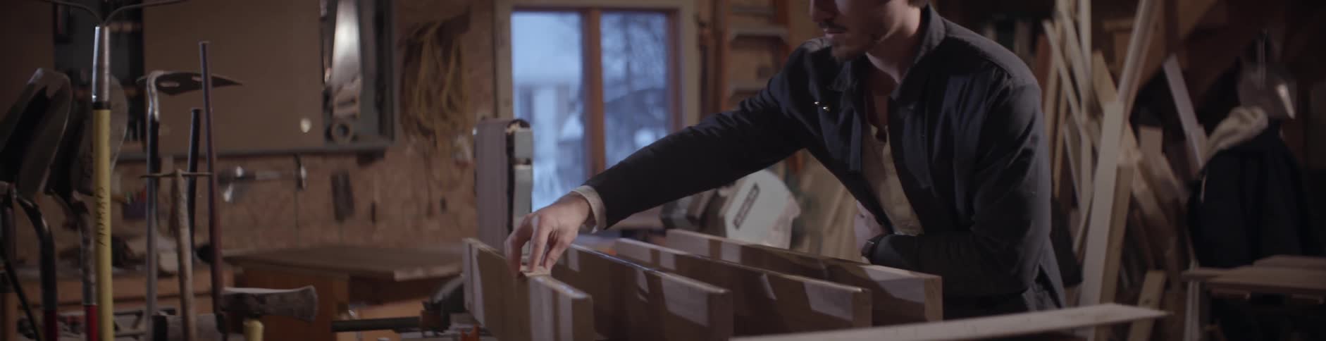 A man picks up a piece of wood and blows dust off of it