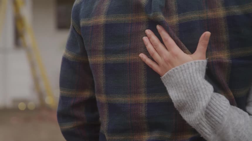 The video shows a closeup of a womans hand resting on a mans back the woman is wearing a gray sweater and the man is wearing a plaid flannel shirt
