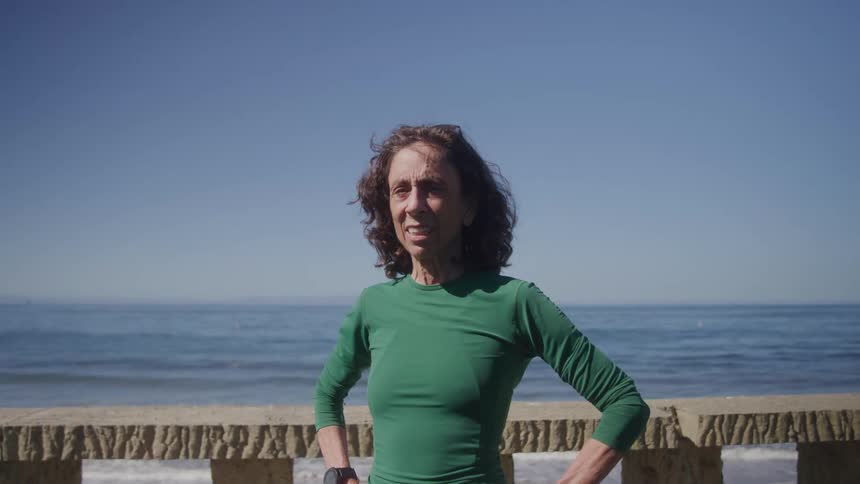 A woman stands confidently near the ocean under a clear blue sky