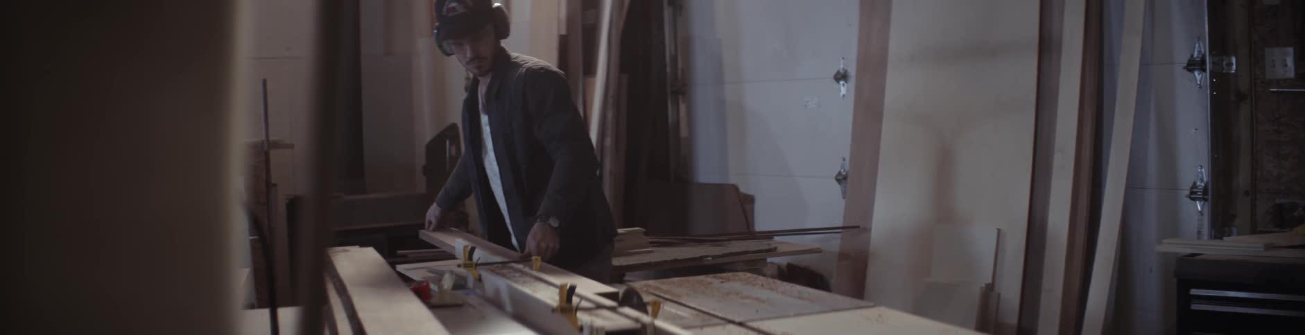 A man examines a piece of lumber and then cuts it with a saw