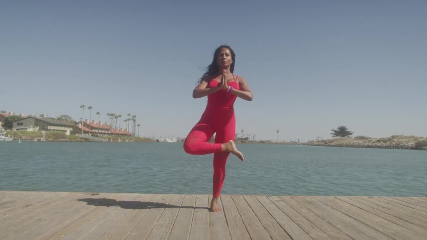 A woman standing on a wooden dock maintains her balance while doing yoga