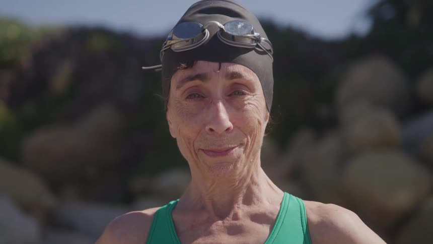 An elderly woman wearing a swimming suit stands in an outdoor pool area