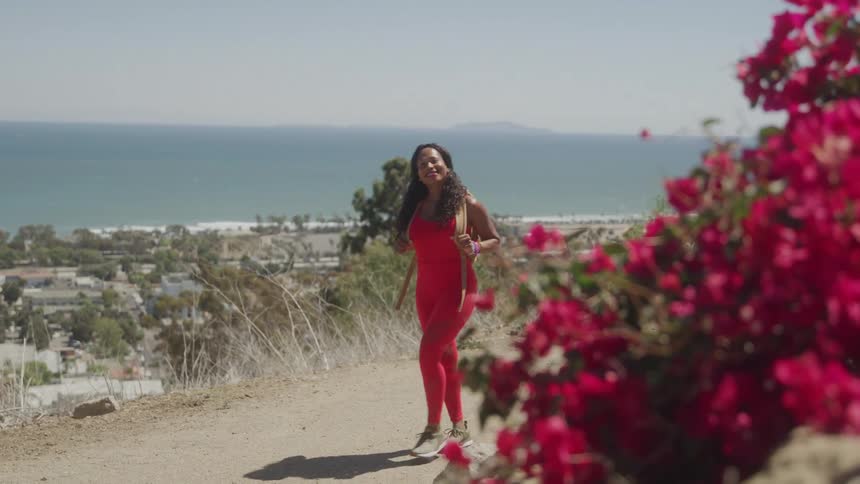 Woman in red outfit walks on a trail overlooking the sea