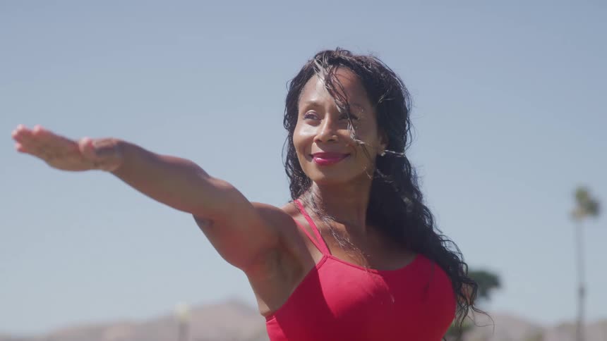 A woman smiles while she maintains a yoga pose while outdoors