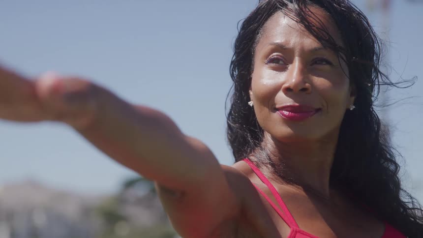 A confident woman in a red top stretches her arm outward while enjoying the sun outdoors