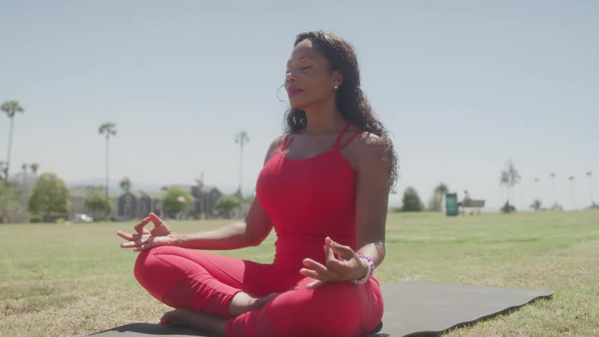 Woman seated in lotus position on a mat practices meditation outdoors on a sunny day