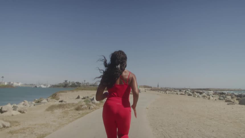 A woman runs on a path beside the beach under the sun wearing red tights
