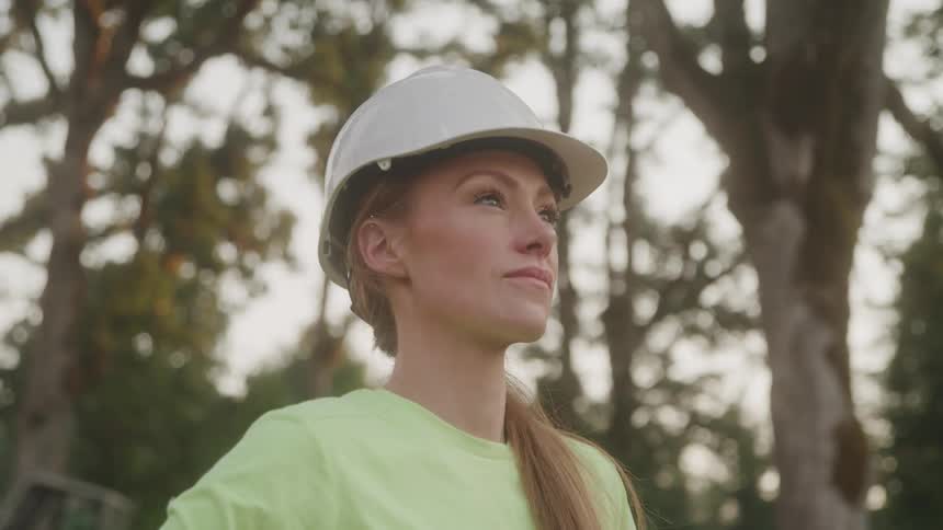 Woman wearing a white safety helmet and green shirt looks forward confidently
