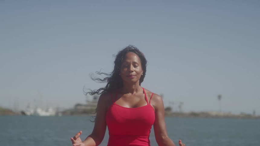 A woman wearing a red dress sits outdoors meditating at midday