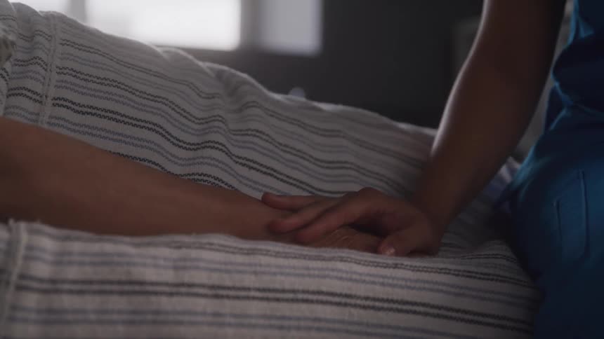 A person lies on the bed with a child sitting beside them inside a bedroom at midday