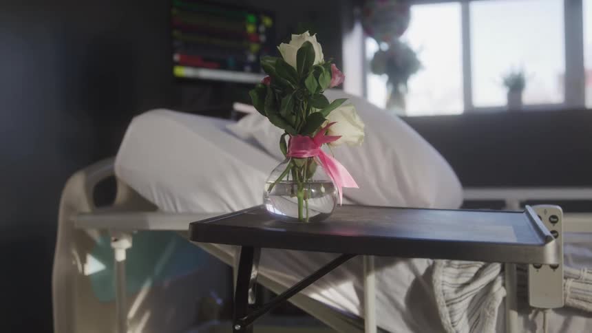 A vase of flowers sits near a hospital bed