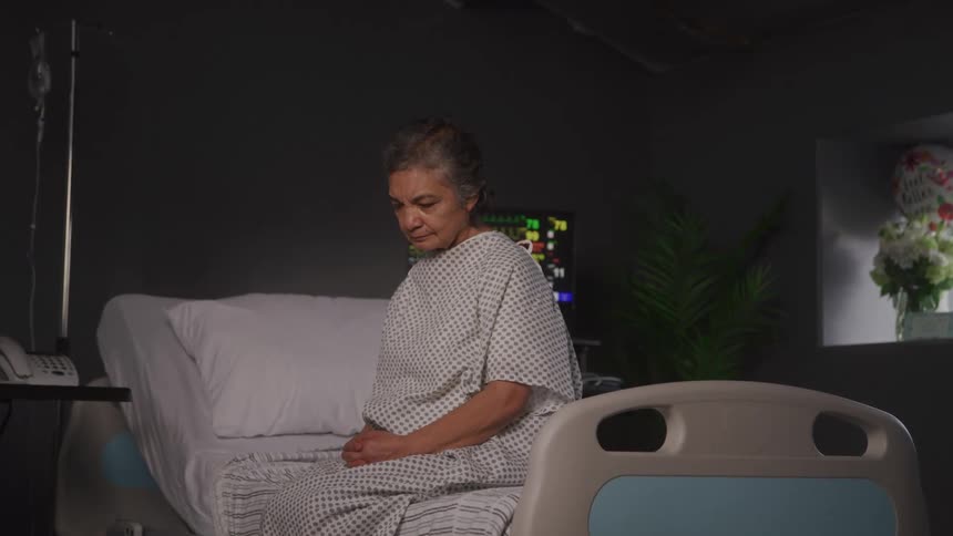 Elderly woman sitting on a hospital bed with her head down