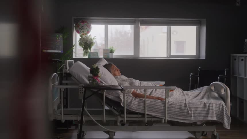 An elderly female patient sleeping on a bed in a hospital room during daytime