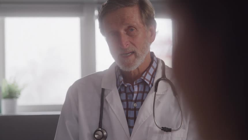 Doctor in a white coat with a stethoscope talks in a bright office