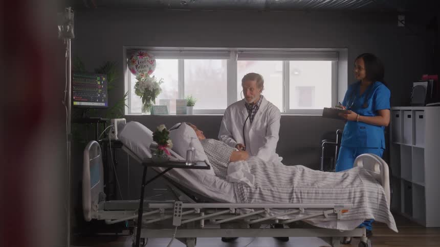 A doctor tends to a patient on a hospital bed at midday with a nurse standing nearby