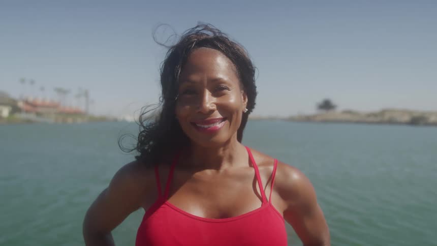 Woman in a red swimsuit smiles by the water on a sunny day