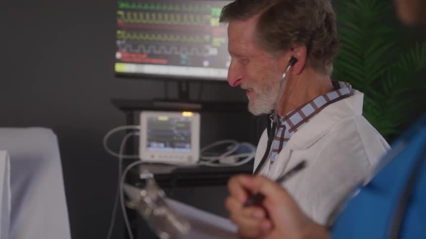 A professional and collaborative closeup shot of two medical professionals in a hospital room with an older male doctor smiling and discussing a patients chart with a female colleague
