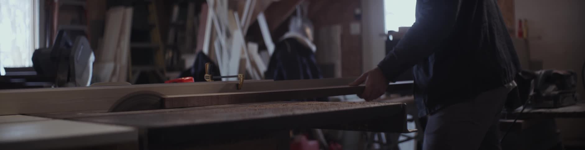 A man slides a piece of lumber onto a workshop table