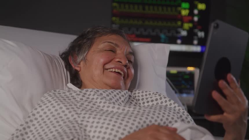 Patient in hospital bed smiles holding tablet