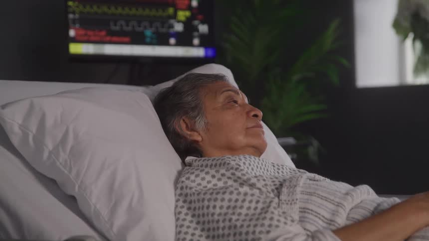 An elderly woman lies in a hospital bed