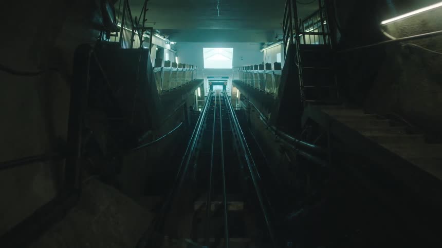 First person view of travelling along tracks through a tunnel and then making a steep incline in an enclosed area surrounded by rails
