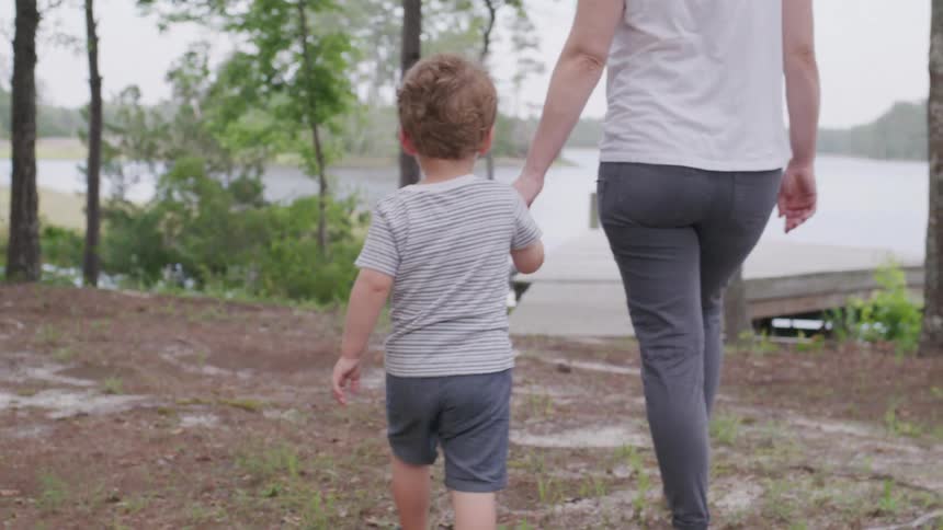 Child holding hands with an adult walks toward a lake