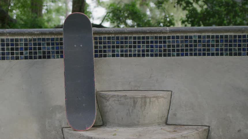 A skateboard is propped against the tiled edge of a concrete seat in an outdoor setting