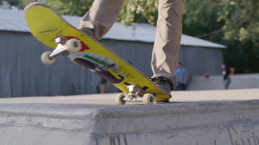 A young man on a skateboard rides toward a ledge at a skatepark while two others watch from a distance