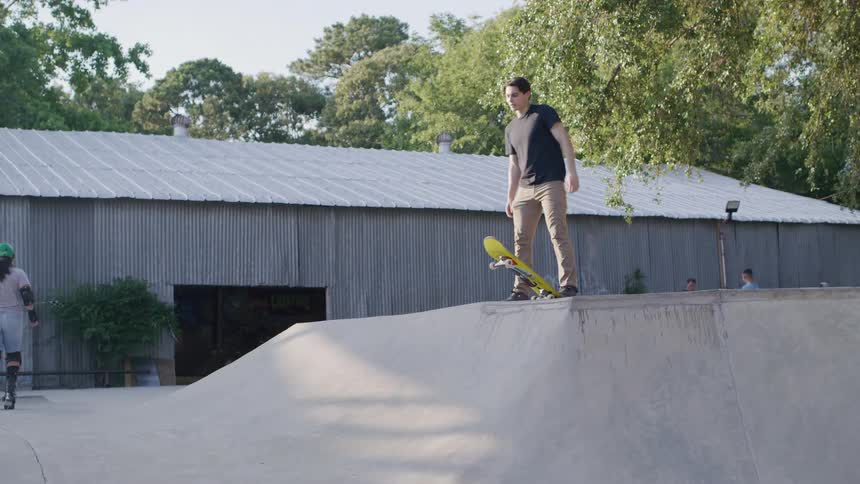 Young man in a black tshirt gets ready to ride down the ramp with a yellow skateboard