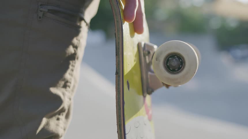 Person holds a yellow skateboard by the truck while walking