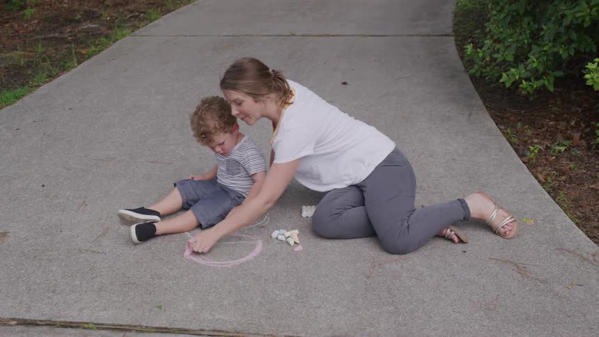 A woman and child enjoy playtime drawing with chalk on the sidewalk