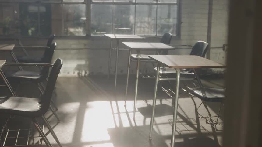 Sunlight streams through large windows illuminating a classroom filled with empty student desks and chairs