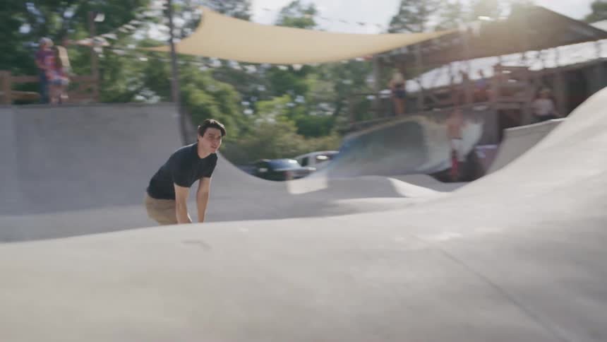 A male skateboarder in a black shirt and beige pants rides down a ramp at a skatepark on a sunny day he is the only person shown in the foreground