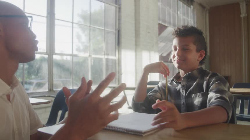 Teacher talks with a student holding a pencil and smiling during class