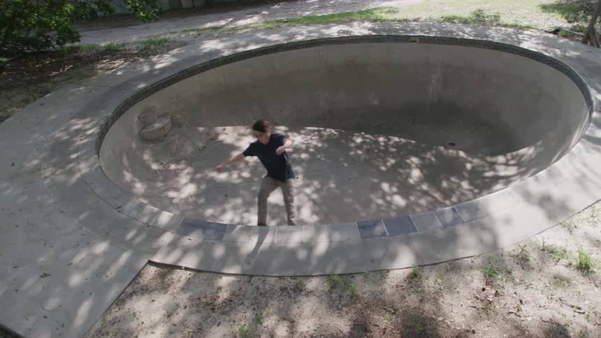 The video shows a person skateboarding in a concrete skate bowl they push off with their foot and ride down the curved side of the bowl