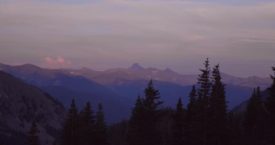 Tall trees lead to a mountain range at sunset