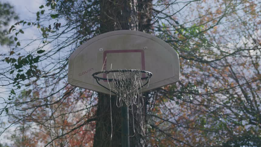 Aged basketball hoop with worn net in an outdoor area surrounded by trees