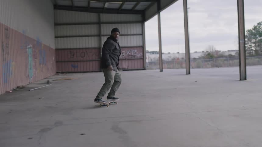 Man doing tricks on a skateboard in a warehouse