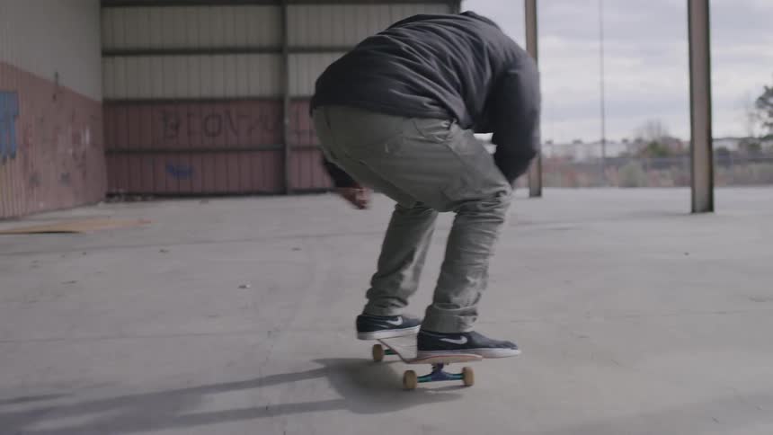 Man skateboarding in the colonnade of a graffiti covered building performs a jump trick