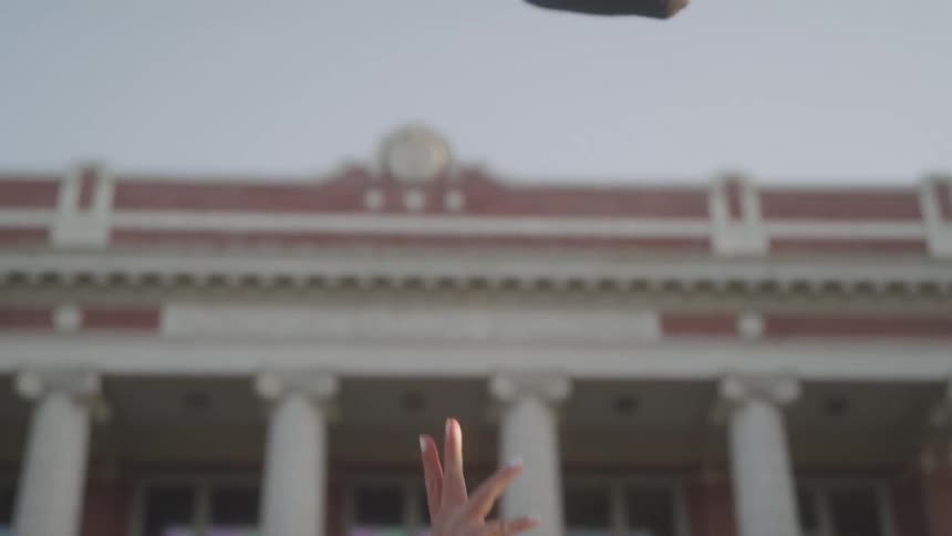 The video shows a person holding a graduation cap and walking their legs are visible as they move with the graduation cap swinging in their hand