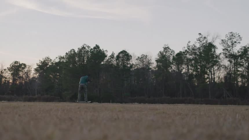 A teenage boy rides a skateboard in a public park at sunset