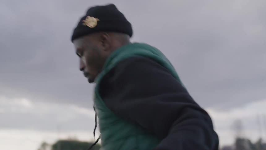 A man in a beanie and vest is actively exercising with a jump rope near a body of water on a cloudy day