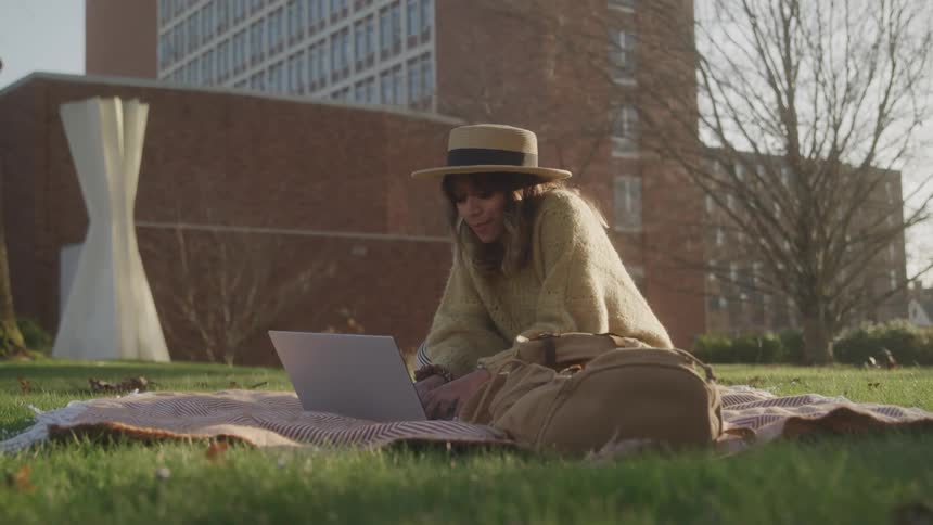 The woman is typing on a laptop while sitting on a blanket