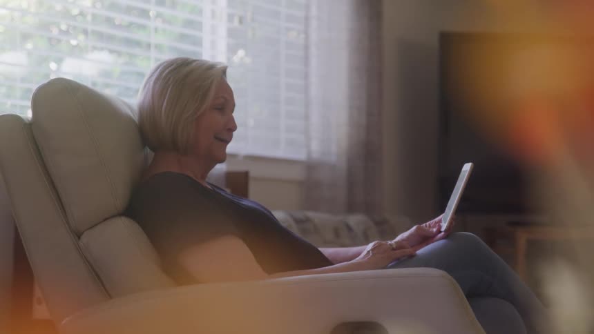 Woman sitting in an armchair reads on a tablet near the window