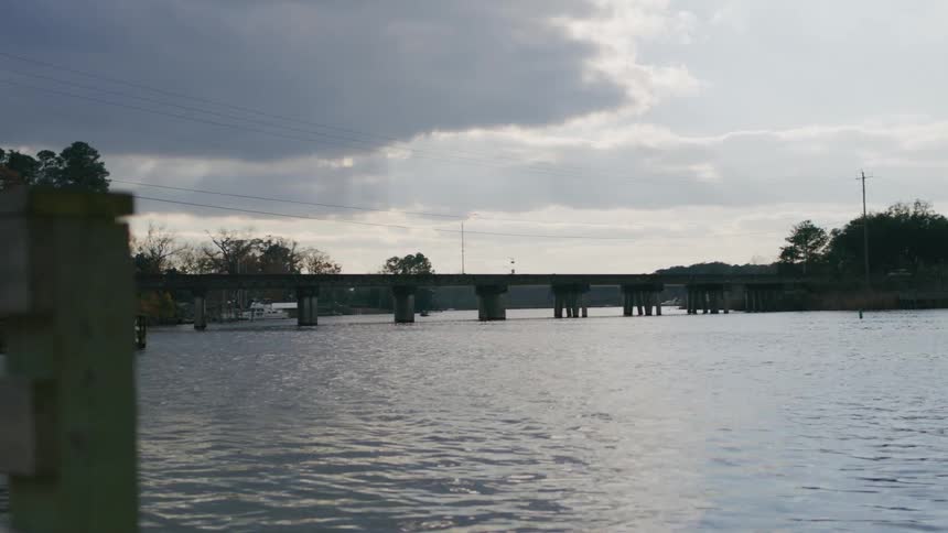 A wooden fence with a red no fishing sign stands at the edge of a calm cloudy river scene