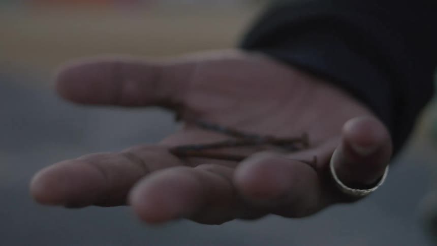 A closeup shot of a persons hand with a ring on their finger holding some small dark objects the person then opens their hand to reveal a few metal nails or screws