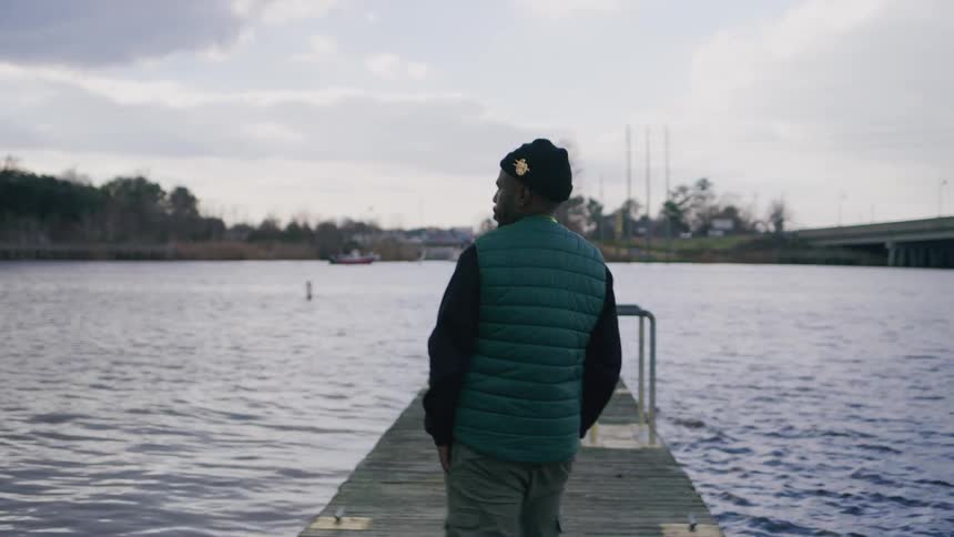 A young man wearing a jacket walks on a dock at midday