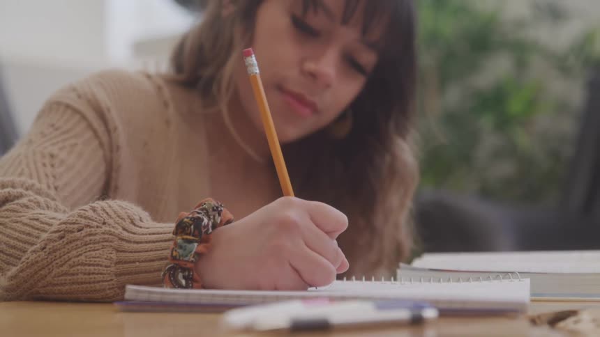 Young woman writes in a notebook with a pencil while studying at a table