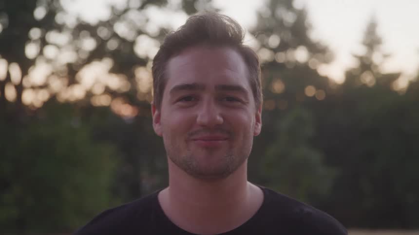 Man in a black tshirt smiles outdoors at sunset