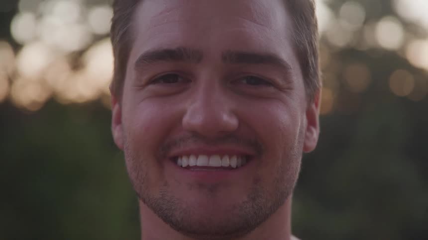 Young man smiles in a closeup outdoors during sunset